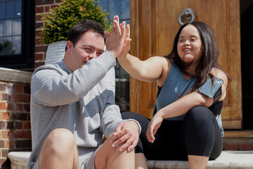 Young biracial couple with Down Syndrome in active wear and wearable tech high-fiving - Powered by Adobe