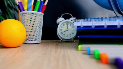 student home office table with white alarm clock, books, orange, colored notebooks, pencils in glass, chalk board, globe, white alarm clock, concept of education, back to school, knowledge day