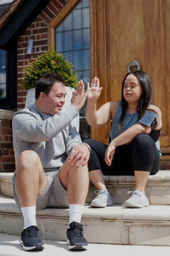 Young biracial couple with Down Syndrome in active wear and wearable tech high-fiving