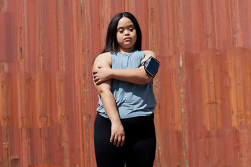 Young biracial woman with Down Syndrome in active wear and wearable tech stretching her arms