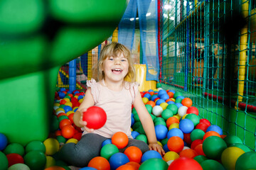 Active little girl playing in indoor playground. Happy joyful preschool child climbing, running, jumping and having fun with colorful plastic balls. Indoors activity for children.