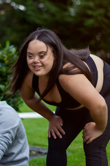 Fototapeta premium Young biracial woman with Down Syndrome in active wear stretching and smiling