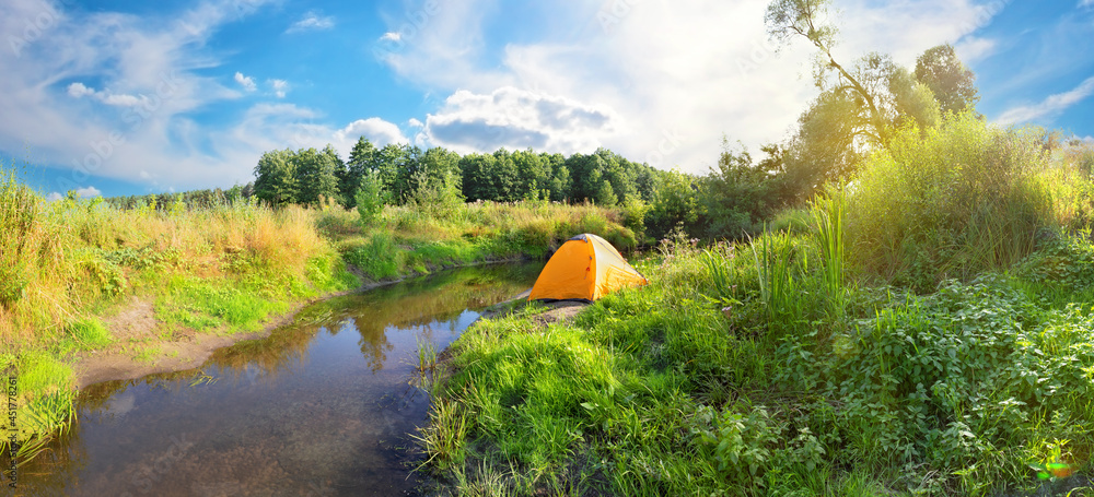 Wall mural orange tourist tent on bank of river with banks