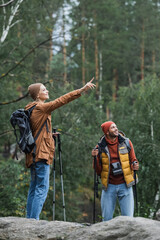 Fototapeta na wymiar happy woman pointing with finger near boyfriend trekking in forest