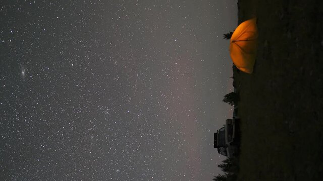 Two travelers watching the meteor shower in summer time. Timelapse of stars moving in night sky over the camp tent