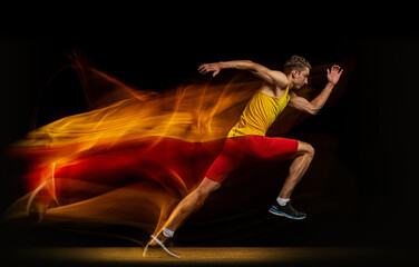 Portrait of young man, professional male athlete, runner in motion and action isolated on dark background. Stroboscope effect.
