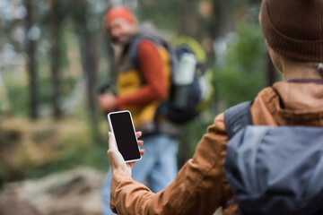 woman holding smartphone while blank screen near blurred man in forest