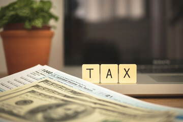 TAX word on wooden blocks and 1040 application form on desktop with laptop and dollar bills. Taxation concept photo