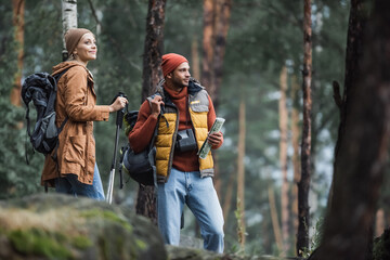 man holding map near cheerful woman with hiking sticks