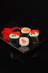 Sushi roll with reflection on a black background. Japanese kitchen and restaurant. Dark sushi rolls with red salmon caviar.