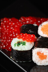 Sushi roll with reflection on a black background. Japanese kitchen and restaurant. Dark sushi rolls with red salmon caviar.