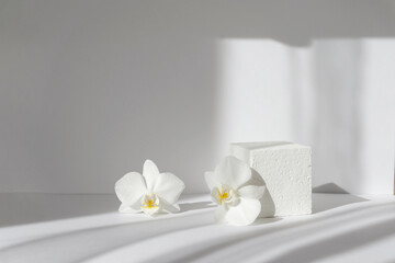 Geometric white 3d podium for presentations of packaging and cosmetics. Foam cube surrounded by orchid flowers in rays of morning sunlight
