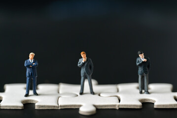 Miniature people Group Business man mini figures standing thinking on Jigsaw Puzzle black background with copy space using as thinking business plan and how to solve problem Strategy Planning concepts