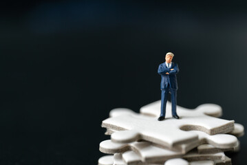 Miniature people Group Business man mini figures standing thinking on Jigsaw Puzzle black background with copy space using as thinking business plan and how to solve problem Strategy Planning concepts