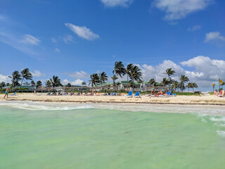 Cayo Coco, Cuba, May 16, 2021: Nice view of the sandy beach with turquoise water and palm trees. People are resting by the ocean.