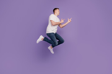 Fototapeta na wymiar Profile photo of positive crazy adviser guy jump indicate fingers empty space on purple wall