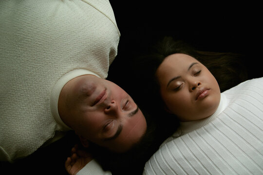 Portrait of young biracial couple with Down Syndrome lying next to each other with closed eyes