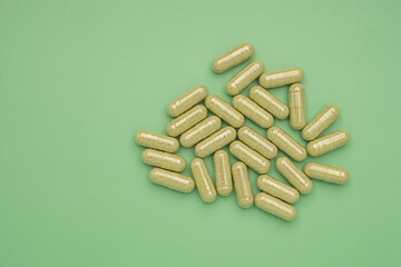 Flat lay of Andrographis paniculata capsules isolated on a green background. Space for text. Herbal, medicine, and healthcare concept