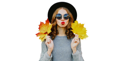 Autumn portrait of beautiful young woman model posing with yellow maple leaves blowing her lips wearing a black round hat, gray knitted sweater isolated on white background