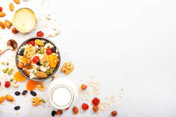 Muesli bowl and ingredients for healthy breakfast. Granola, nuts, dried fruits, flakes, honey and greek yogurt on white table copy space