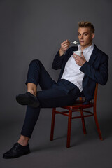 young guy in a blue suit and white shirt posing while sitting in the studio on a gray background with yogurt and a spoon in his hands