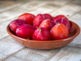 Ripe honey red plums in a ceramic plate, close-up
