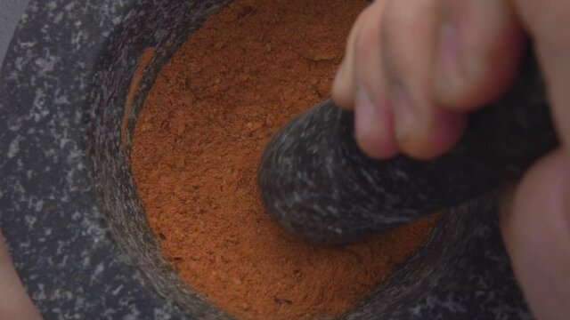Super close-up of hand with pestle grinding and mixing spices and peppers