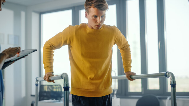 Hospital Physical Therapy: Portrait of Strong Male Patient with Injury Successfully Walks Holding Parallel Bars. Physiotherapist, Rehabilitation Doctor, Help, Assist, Disabled Person.
