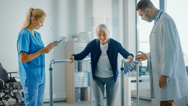 Hospital Physical Therapy: Portrait of Strong Senior Female Patient with Injury Successfully Walks Holding Parallel Bars. Physiotherapist, Rehabilitation Doctor, Help, Assist Disabled Patient