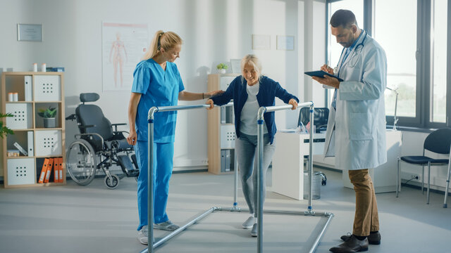 Hospital Physical Therapy: Portrait of Strong Senior Female Patient with Injury Successfully Walks Holding Parallel Bars. Physiotherapist, Rehabilitation Doctor, Help, Assist Disabled Patient