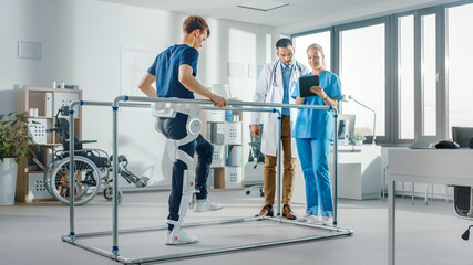 Modern Hospital Physical Therapy: Patient with Injury Walks Wearing Advanced Robotic Exoskeleton. Physiotherapy Rehabilitation Scientists, Engineers use Tablet Computer to Help Disabled Person