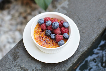 Tasty creme brûlée with heath-berry and raspberry. Creme brûlée dessert with blueberries. Close up. Fresh homemade creme brûlée with burnt sugar isolated on white background. Selective focus 