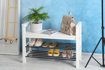 Shelving unit with stylish shoes and mirror near light blue wall in hall
