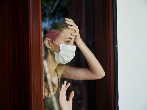 woman in medical mask upset looking out the window