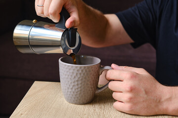 A man pours coffee from a stylish moka pot into a cup. Equipment for making coffee. Professional coffee brewing. Morning coffee for breakfast. Aromatic black coffee in a cup close-up