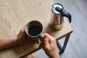 A man drinks delicious black coffee made in a moka pot coffee maker. Professional coffee brewing. Morning drink for breakfast. Fragrant black coffee in a cup close-up. Equipment for making coffee