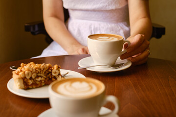 A woman with a cup of aromatic coffee and a sweet nut cake sits in a cafe or restaurant. The girl drinks a hot latte or cappuccino after breakfast with a delicious dessert.