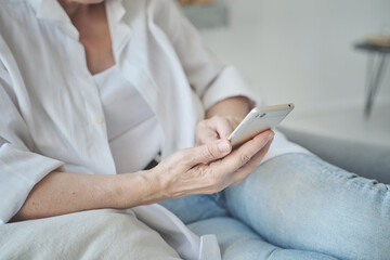 Close-up of an old lady using a smartphone app to read uplifting news, the issue of smartphone...