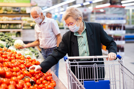 mature woman in mask and gloves with covid picks tomatoes in vegetable section of supermarket