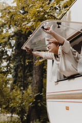 Young woman opening camping van window in the morning in autumn forest.