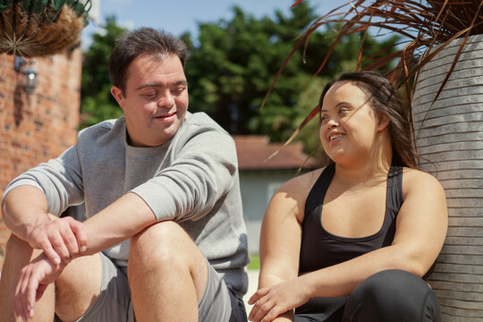 Young biracial couple with Down Syndrome in active wear sitting next to each other and smiling