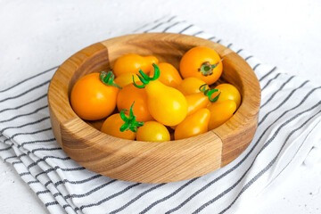 Small yellow tomatoes in wooden bowl on white background. Closeup image of yellow pear tomatoes. Organic healthy food.