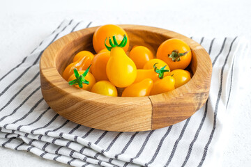 Small yellow tomatoes in wooden bowl on white background. Closeup image of yellow pear tomatoes. Organic healthy food.