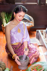 Thai Asian women dressed in ancient Thai costumes from the Ayutthaya period are pounding chili paste and preparing savory dishes in a wooden household.