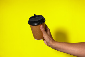 Close-up on a yellow background, a woman's hand holds a paper cup with coffee in a stand. Coffee or tea with you, coffee delivery on a yellow background