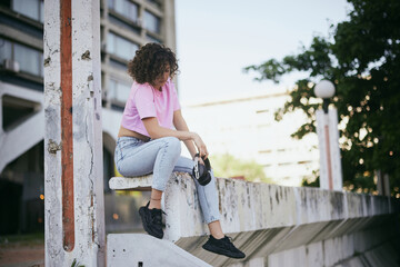 An attractive young woman with curly hair sitting outdoors and holding headphones in her hands. Urban living concept.