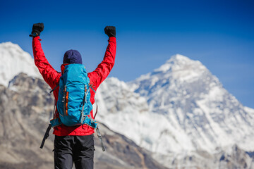 Hiker cheering elated and blissful with arms raised in the sky after hiking. Everest mountain on...