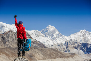 Hiker cheering elated and blissful with arms raised in the sky after hiking. Everest mountain on...