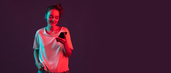 Portrait of pretty romantic girl with phone, gadgets isolated on dark purple studio background in...