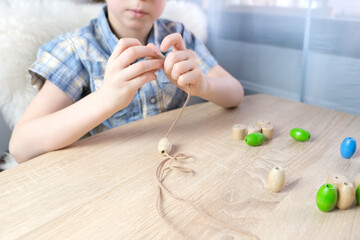 small child, kid stringing colored wooden beads on a string, children's fingers close-up, concept...